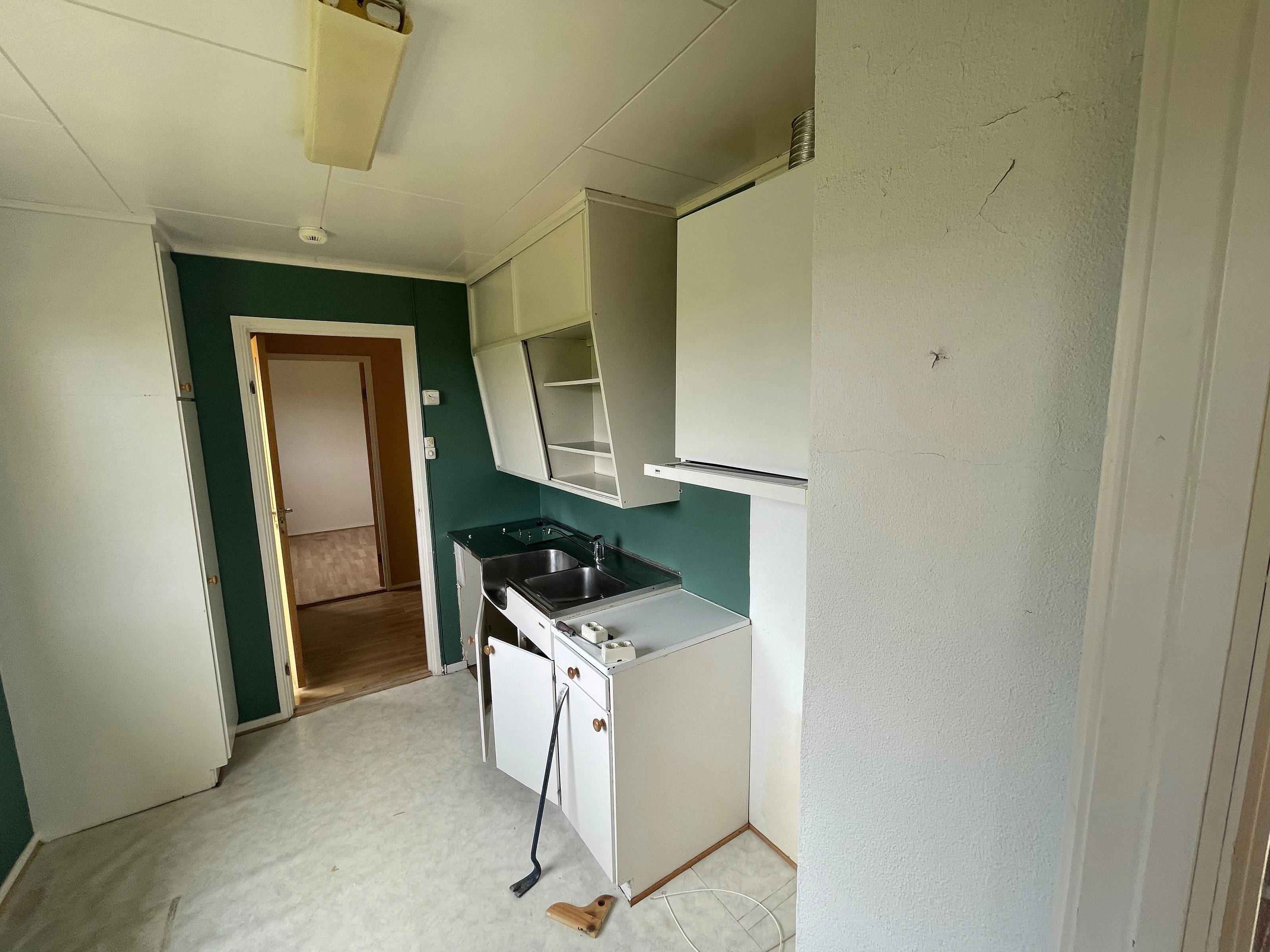 Old kitchen before renovation, with cabinets mid-demolition and a crowbar on the floor.