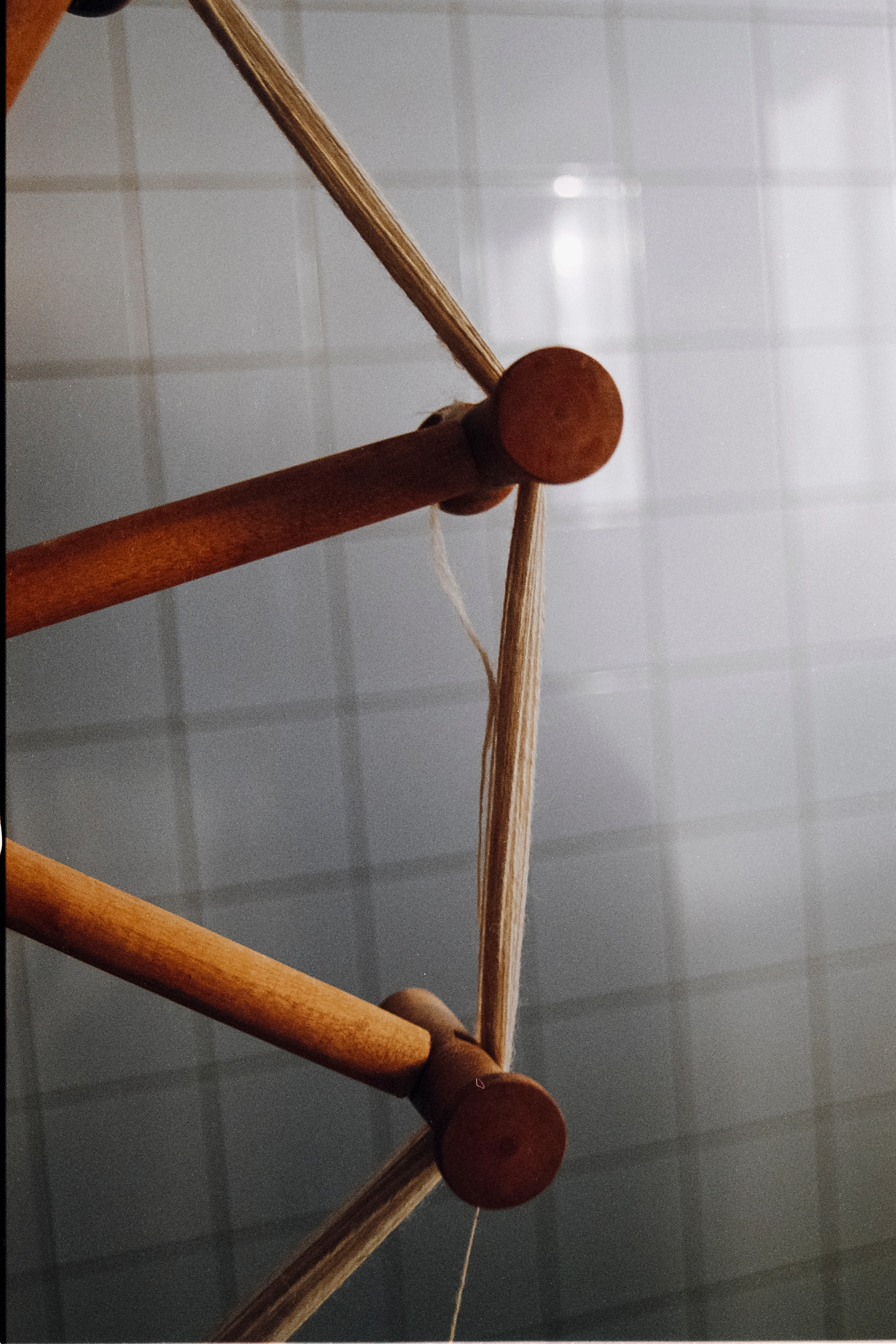 Close-up of a wooden yarn swift with a thin wool thread wound around the wooden pegs, tiled wall in the background.